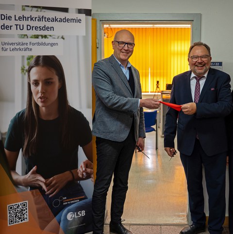 Zwei Männer stehen vor einer geöffneten Tür und halten ein Stück rotes Band in der Hand