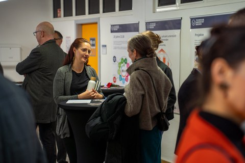 Zwei Frauen im Gespräch an einem Stehtisch, drum herum herrscht buntes Treiben.