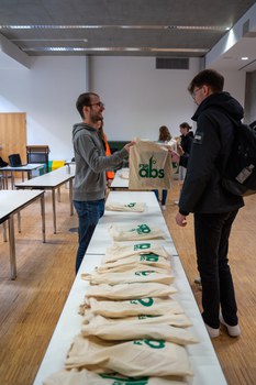 Student übergibt Campusbeutel einem anderen Studenten