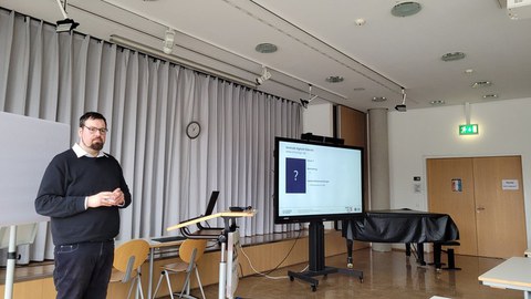 Ein Dozent mit einem in den Unterrichtsraum gerichteten Blick steht neben einer digitalen Tafel.