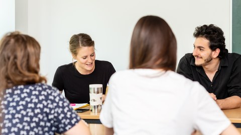 Foto von vier Personen, die sich an zwei Tischen gegenübersitzen und sich unterhalten.