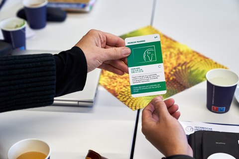 Zwei Hände halten gleichzeitig einen Spielkarte, auf der in englischer Sprache etwas zu Nachhaltigkeit erklärt wird.