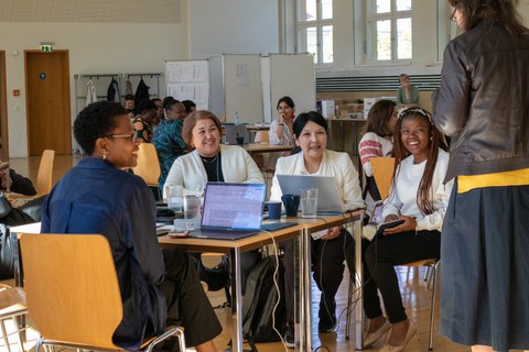 Eine Gruppe von erwachsenen Personen an einem Tisch, die einem Vortrag zuhören.