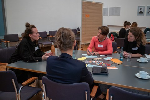 Gruppe von vier Frauen sitzt an einem Tisch und diskutiert miteinander.