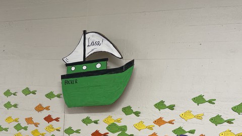 Wand in einer Schule, die mit vielen Zetteln in Fischform beklebt ist.