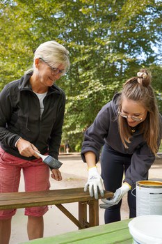 Zwei Frauen arbeiten mit Lack an einer Holzbank