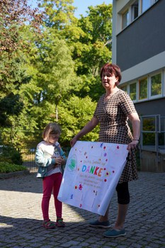 Frau steht mit einem Kind und zeigt eine Dankeschön-Plakat einer Kita