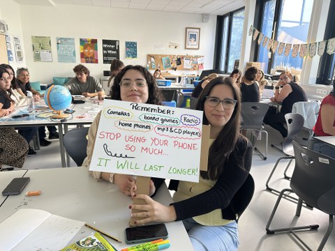 2 Studierende halten ein Schild hoch auf dem steht, dass man das Smartphone nicht so viel nutzen sollte, damit es länger hält.