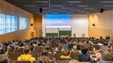 Eine Vortragende steht vor einem komplett gefüllter Hörsaal