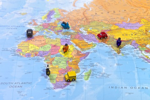 Bild einer Weltkarte. Es sind nur die Kontinente Afrika, Asien und Europa zu sehen. Sieben Miniatur-Fahrzeuge (Auto, Bus, Roller) stehen verteilt auf der Karte.