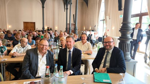 Auf dem Bild sieht man die Diskussionsteilnehmenden Prof. Dr. Axel Gehrmann, Michael Kretschmer und Christian Piwarz an einem Tisch sitzend beim Gewerkschaftstag des Sächsischen Lehrerverbandes am 23. August 2024.