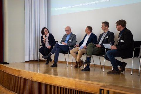 Foto: Fünf Personen sitzen auf Stühlen auf einer Bühne und sind im Gespräch.