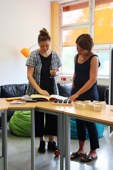 Zwei Kolleginnen erkunden inklusive Materialien wie beispielsweise ein Kinderbuch zu Diversity bzw. ein Fühlpärchen-Spiel.