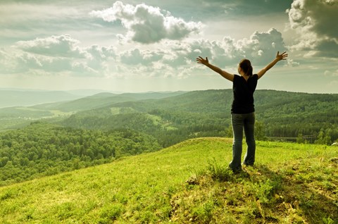 Eine junge Frau steht glücklich auf einem Berg und hebt die Arme