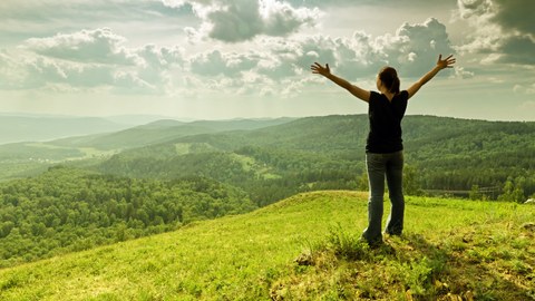 Eine junge Frau steht glücklich auf einem Berg und hebt die Arme