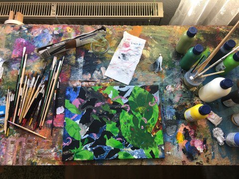 Das Bild zeigt einen Tisch, auf dem das Acrylgemälde "Layers" der Studentin Selina Münning sowie ein Pinsel, Farben und weitere Materialien liegen.