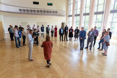 Das Foto zeigt ca. 25 Personen, die in einem Festsaal in kleineren Grüppchen stehen.