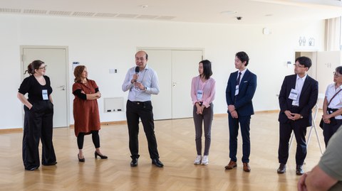 Das Foto zeigt sechs Personen, die nebeneinander stehen. Eine Person hält ein Mikrofon in der Hand.