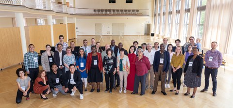 Das Foto zeigt eine Gruppe von ca. 30 Personen unterschiedlicher Herkunft in einem Saal, die sich zum einen Gruppenbild aufgestellt haben. 