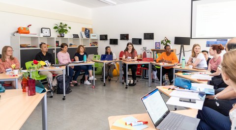 Das Foto zeigt eine Gruppe von ca. 10 Personen, die auf Bestuhlung in U-Form sitzen und an einem Workshop teilnehmen