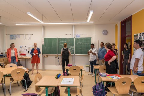 Das Foto zeigt eine Gruppe von Erwachsenen, die sich in einem Klassenzimmer umsehen.