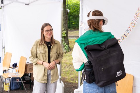 Das Foto zeigt eine junge Frau, die einer anderen Frau eine VR-Brille erklärt, während sie sie ausprobiert.