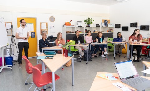 Das Bild zeigt mehrere Personen in einem Raum, während eines Workshops. Auf der linken Seite ist der Moderator des Workshops zu sehen.