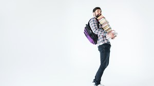 Bild eines Mannes mit Rucksack, der vor einem weißen Hintergrund steht und einen großen Stapel Bücher mit beiden Händen trägt.