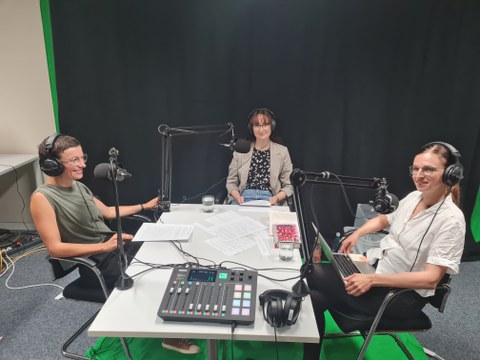 Drei Frauen sitzen um einen Tisch herum, während sie einen podcast aufnehmen.