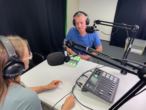 Mann sitzt an einem Tisch mit Podcastequipment während einer Aufnahme