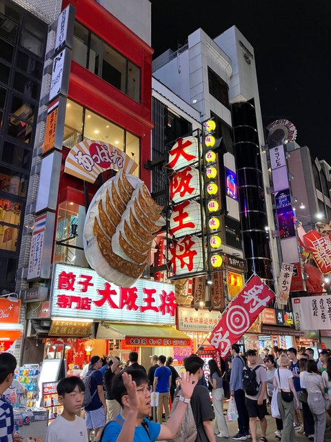 Das Foto zeigt eine belebte japanische Fußgängerzone am Abend mit vielen bunten Werbeschildern.