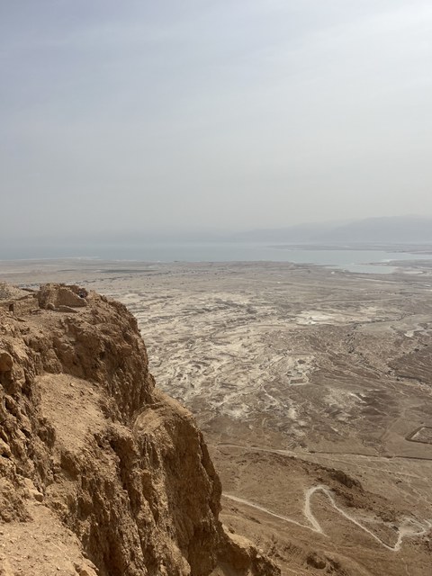 Das Foto zeigt eine felsige braune Landschaft, im Hintergrund ist eine Stadt am Meer zu erkennen.