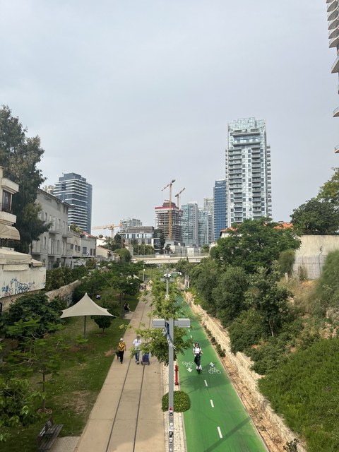 Foto einer Großstadt von weitem. Im Vordergrund ist ein Fuß- und Radweg zu sehen.