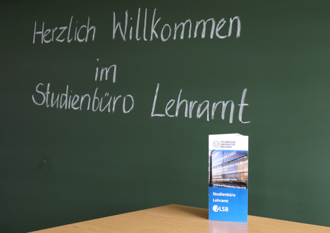 Das Foto zeigt eine Tafel, auf der "Herzlich Willkommen im Studienbüro Lehramt" geschrieben steht. Auf der Unterkante der Tafel steht eine Informationsbroschüre des Studienbüros Lehramt.