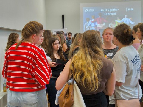 Foto von Personen, die sich intensiv Austauschen. Im Hintergrund ist die Projektion der Folie GetTUgether Lehramt zu sehen. 