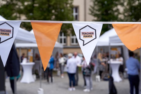 Ein Wimpel im Vordergrund, wo "TEACHERMANIA" draufsteht, im Hintergrund herrscht buntes Treiben