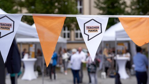 Ein Wimpel im Vordergrund, wo "TEACHERMANIA" draufsteht, im Hintergrund herrscht buntes Treiben