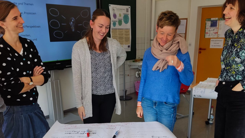 Foto: Vier Personen stehen rund um einen Tisch, auf dem ein Plakat mit handschriftlichen Notizen liegt.