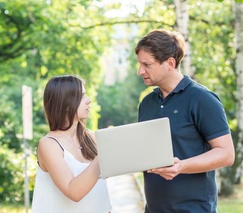 Foto von zwei Personen im Freien, die ein Laptop halten.