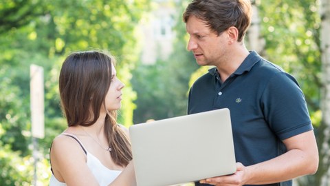 Foto von zwei Personen im Freien, die ein Laptop halten.