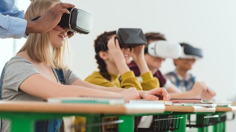 Foto: Kinder sitzen an Tisch und tragen VR-Brillen
