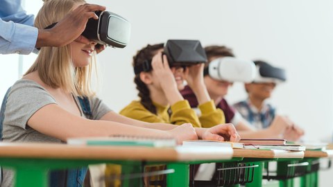 Foto: Kinder sitzen an Tisch und tragen VR-Brillen