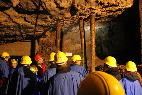 Foto: Personengruppe vor einer Felswand in einem Bergwerk. Alle tragen blaue Jacken und gelbe Schutzhelme.