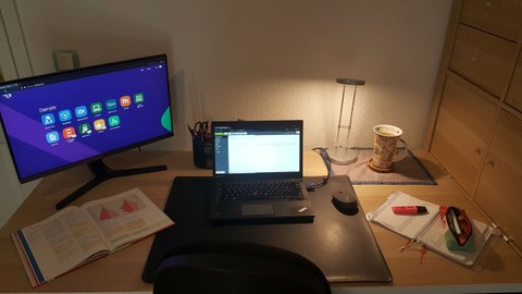 Foto: Schreibtisch mit Bildschirm, Laptop, Lampe und anderen Gegenständen