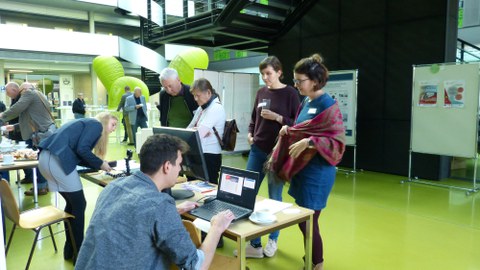 Bild des Foyers des Gebäudes der Fakultät Informatik der TU Dresden. Mehrere Menschen sitzen bzw. stehen an Tischen.