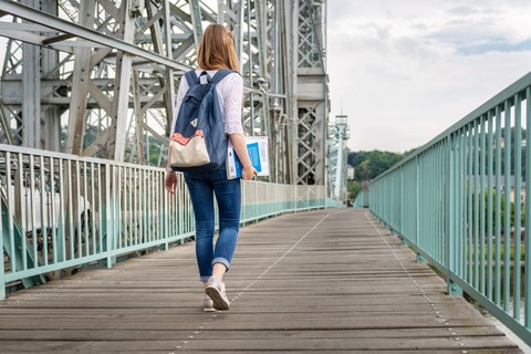 Eine Studentin hält Lernmaterial in der Hand und läuft über das Blaue Wunder.