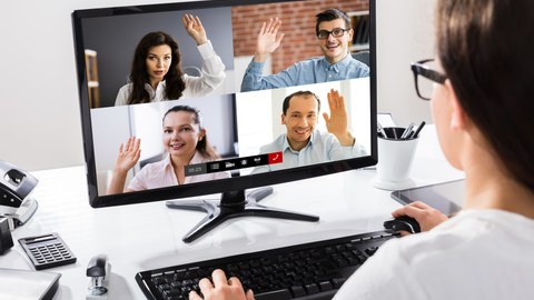 Foto: Eine Person blickt auf einen Bildschirm, auf dem vier Personen in einer Videokonferenz zu sehen sind.