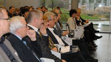 Bild von mehreren Personen, die auf Stühlen in mehreren Reihen sitzen und augenscheinlich einem Vortrag zuhören. Einige Personen haben Unterlagen vor sich auf dem Schoß.