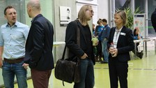 Bild, auf dem vier Personen jeweils zu zweit stehen und sich unterhalten. Im Hintergrund sind weitere Personen zu sehen.