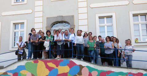 Bild einer Gruppe von Personen, die an dem Geländer vor der Schkola in Ostritz lehnen und in die Kamera lächeln.